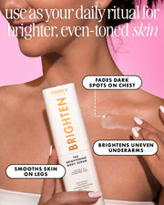 A woman holds a bottle of Truly Brighten The Brightening Body Serum against a pink background, with text overlays describing skin benefits.