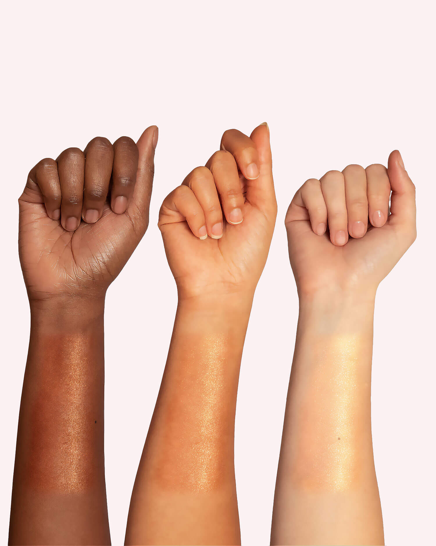Three raised forearms of varying skin tones display swatches of Truly Beauty’s Sun Drops Bronze Body Glow, showcasing its hydrating, shimmery golden finish and sunkissed radiance against a pale background.