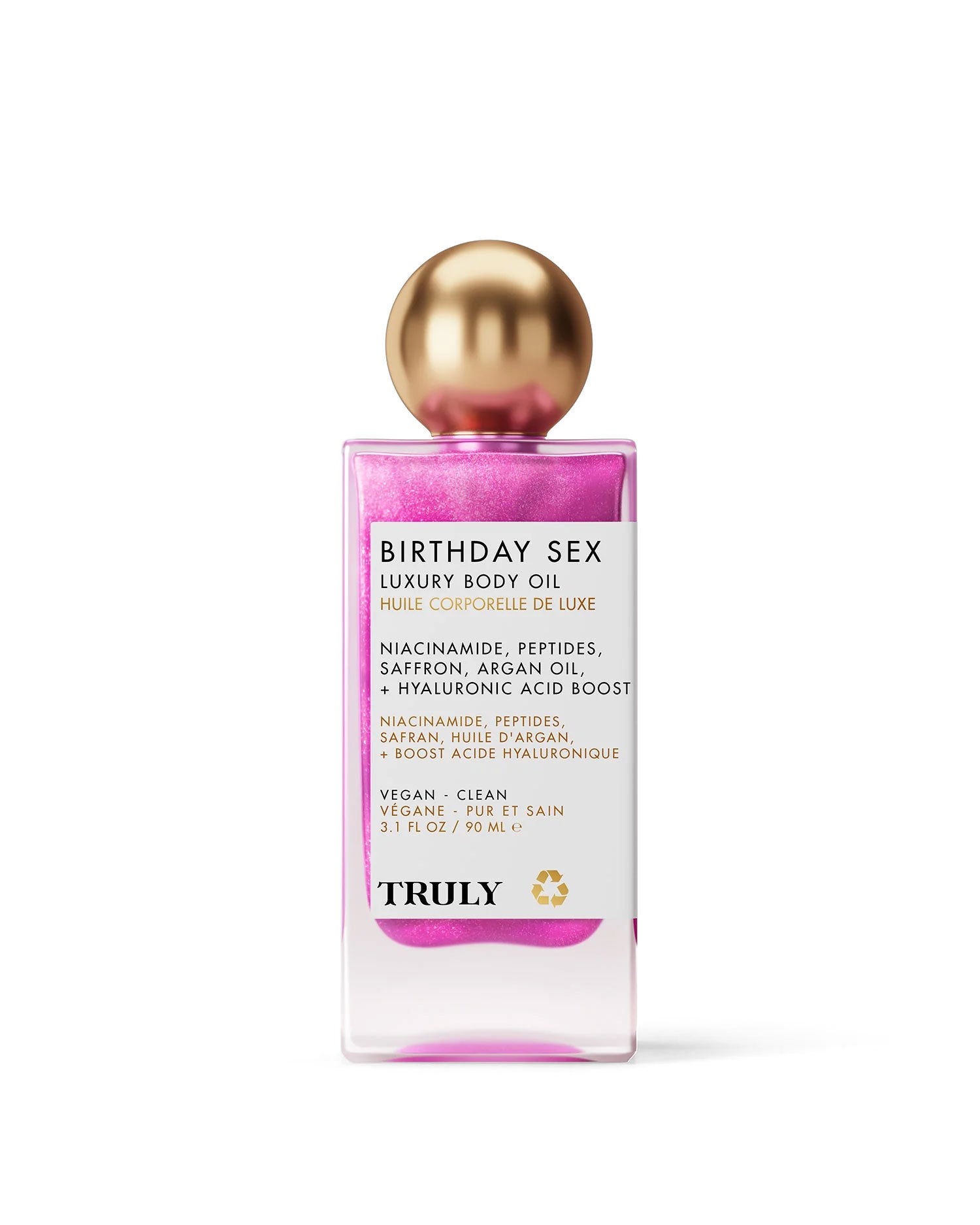 A bottle of Truly Beauty Birthday Sex Luxury Body Oil features shimmering pink liquid, a gold round cap, and a white label highlighting niacinamide, peptides, saffron, argan oil, and hydrating hyaluronic acid.