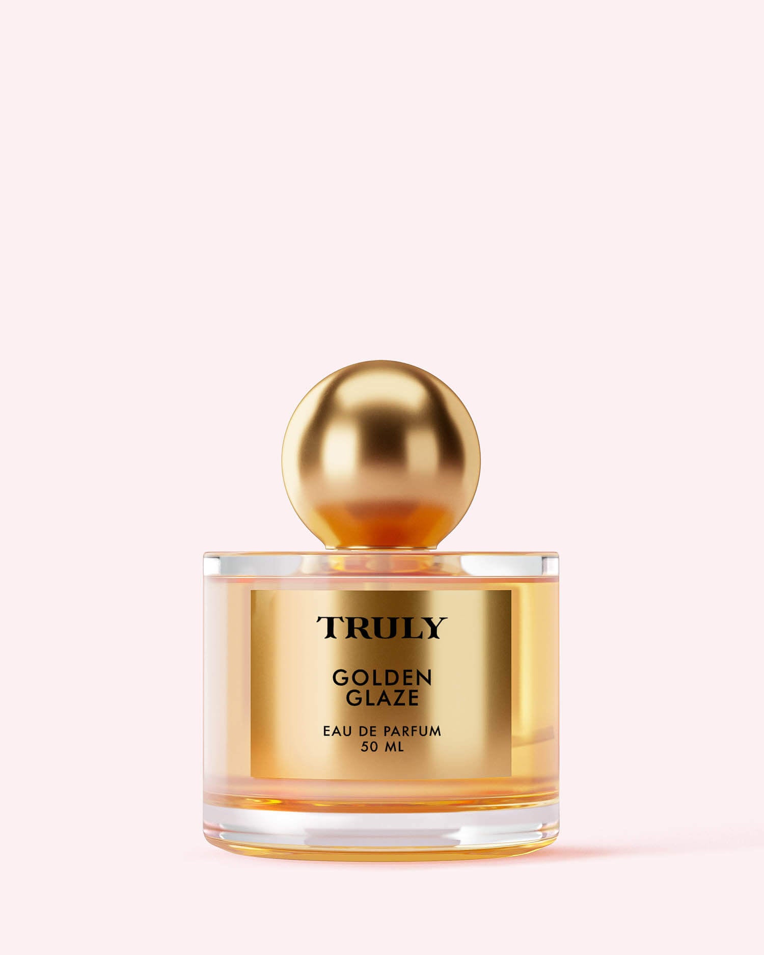 A clear glass bottle labeled Golden Glaze Eau De Parfum by Truly Beauty, 50 ml, with a shiny gold cap set against pale pink hints at the allure of pink pepper in its luxurious fragrance.