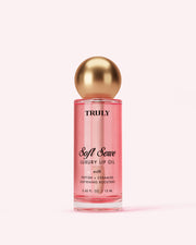 A pink bottle of Truly Luxury Peptide Lip Oils Soft Serve with a gold spherical cap and black/gold text on the label, set against a pale white background.