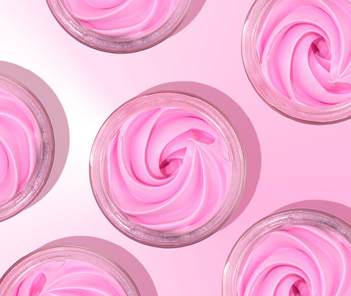 Open jars of Truly’s bright pink, swirled cream are arranged on a pastel pink background, forming a visually pleasing, symmetrical pattern.