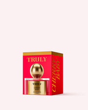 A pink and gold box labeled Truly Beauty Cherry Baby Eau De Parfum holds a bottle with a gold cap and label. The fragrance features black cherry and jasmine notes, displayed on a light pink background.