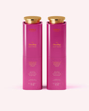 Two tall, pink cylindrical bottles with gold caps, labeled Truly Beauty The Smoothing Body Serum (3.1 fl oz/90 ml), stand side by side against a pale pink background. This serum helps smooth rough, bumpy skin including keratosis pilaris.