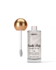 A bottle of Truly Beauty Luxury Peptide Lip Oil with a gold spherical cap and applicator wand sits against a pale white background. The clear bottle reveals the shimmery oil inside.