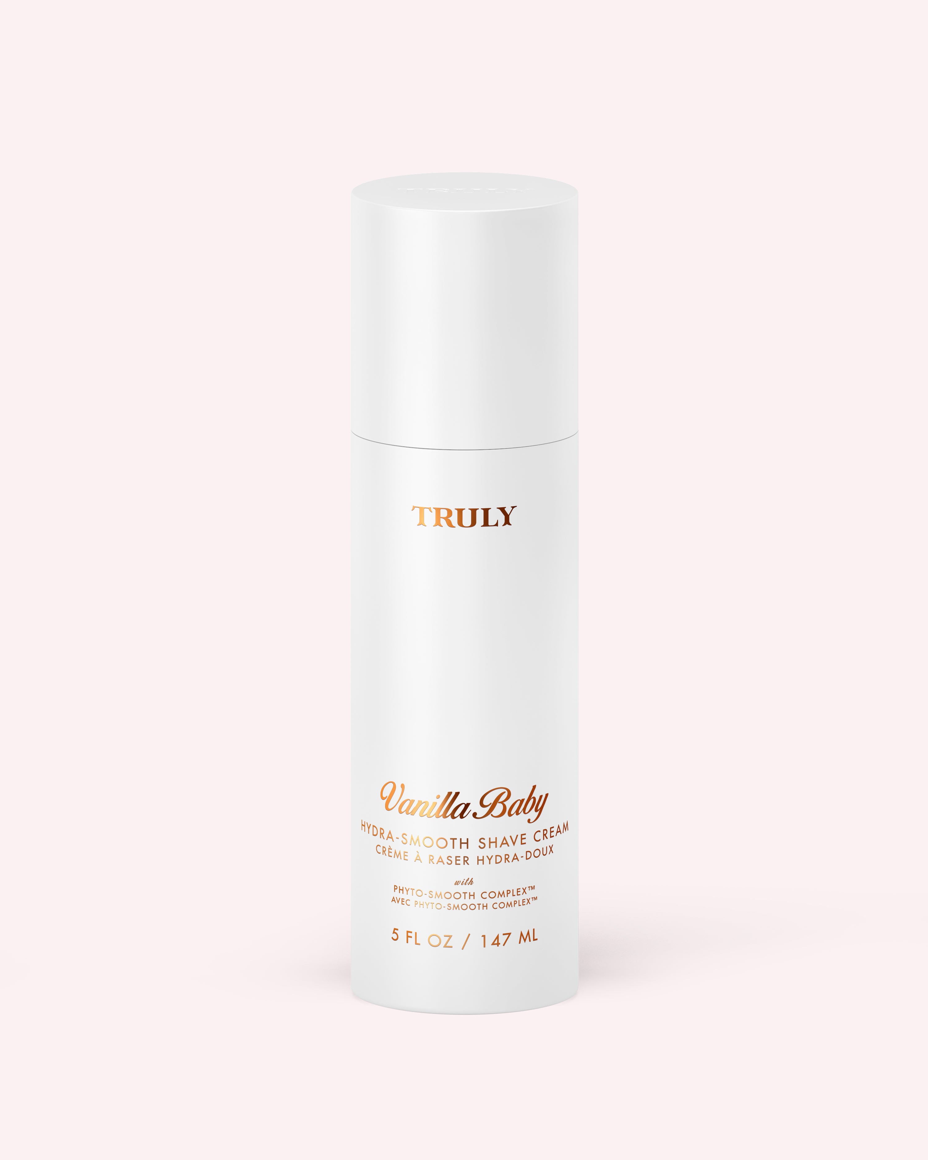 A white cylindrical bottle labeled Hydra-Smooth Shave Cream by Truly Beauty, with gold and peach text, sits on a light pink background. The bottle contains 5 fl oz (147 ml) of product.