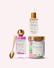 Three Truly Beauty products from Zaras Everyday Routine are displayed: Birthday Sex Luxury Body Oil (pink bottle), Cooka Oil (gold dropper), and Buns of Glowry Butt Butter (clear jar) with a gold spoon, on a pale pink background.