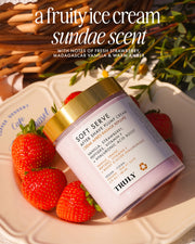 A jar of Truly Beauty’s Soft Serve After Shave Duo sits on a plate with fresh strawberries, highlighting its hydrating formula and fruity ice cream sundae scent with notes of strawberry, vanilla, and amber.