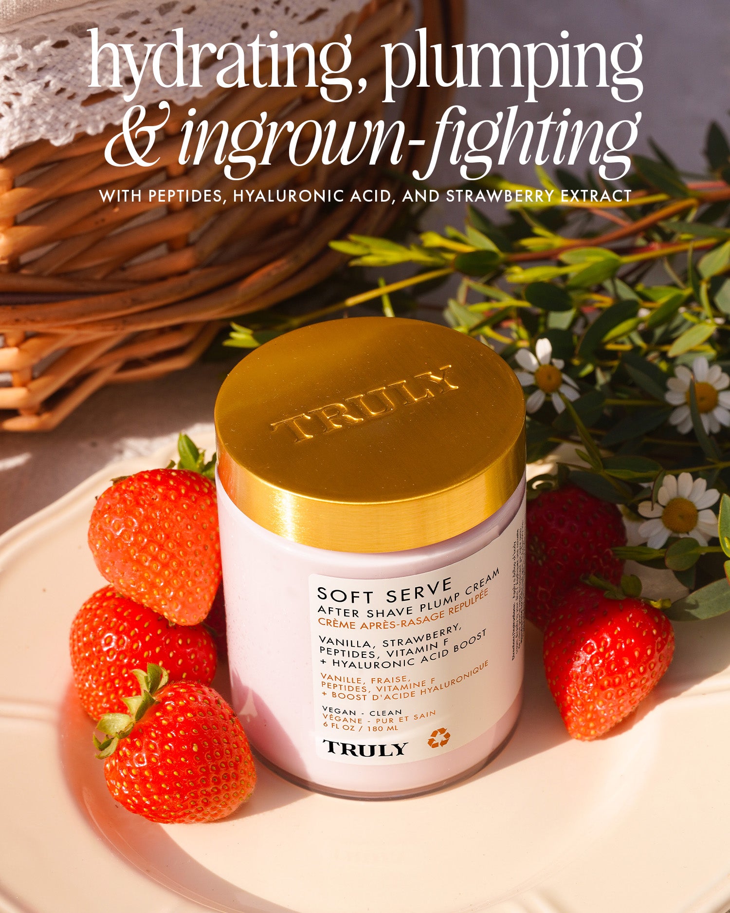 A jar of Truly Beauty Soft Serve After Shave Duo rests on a white plate with strawberries, near a wicker basket and flowers. The label spotlights hydrating peptides, hyaluronic acid, and ingrown-fighting strawberry extract.
