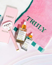 The Smooth Legend - Complete Collection by Truly Beauty features a pink razor, two skincare serums, and a pink TRULY-embroidered towel—the perfect shave kit for your Smooth Legend routine. Razor box and bottles display the Truly Beauty brand.