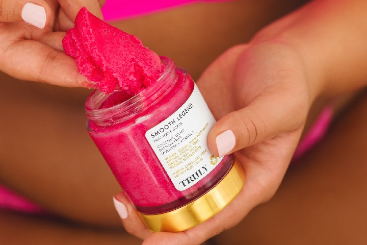A person scoops out pink sugar scrub from glass jar