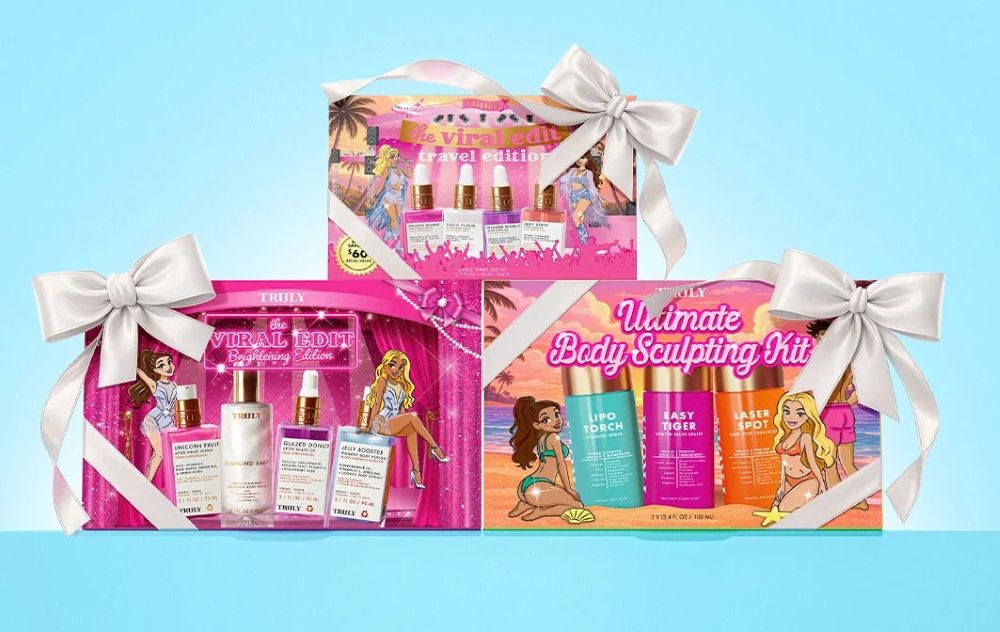 Three Truly Beauty skincare and body care holiday gift sets packaged in pink decorative boxes with white satin bows against a light blue background