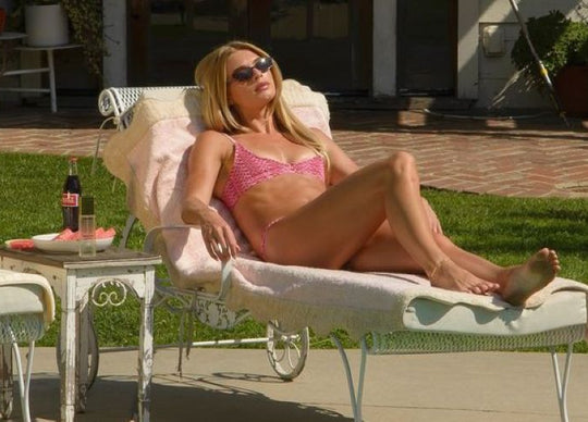 is spf 30 enough | A blonde woman wearing a pink textured bikini and a straw sun hat sits on a lounge chair by a pool, spraying bottle of Truly's Solar Baby SPF 45 Invisible Sunscreen Oil into her hand.