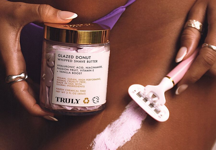 how often should you shave | woman shaving bikini line with pink razor holding Truly's glazed donut shave butter