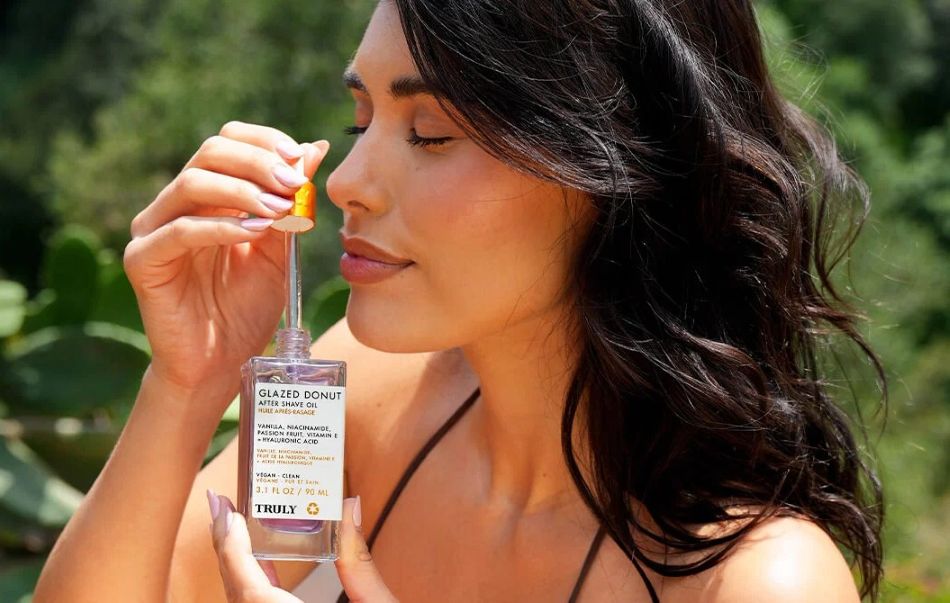 Woman holding a bottle of Truly Glazed Donut Skin Oil in a natural setting