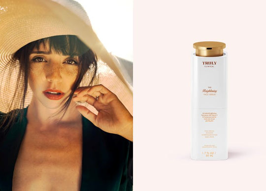 how to brighten dull skin | young woman wearing pink hair curlers poses with bottle of Truly's Diamond Baby Treatment Body Serum with a vintage looking background