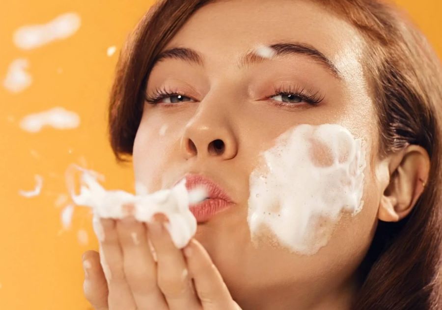 how to remove sunscreen | model with foam cleanser on face blowing cleanser from hands