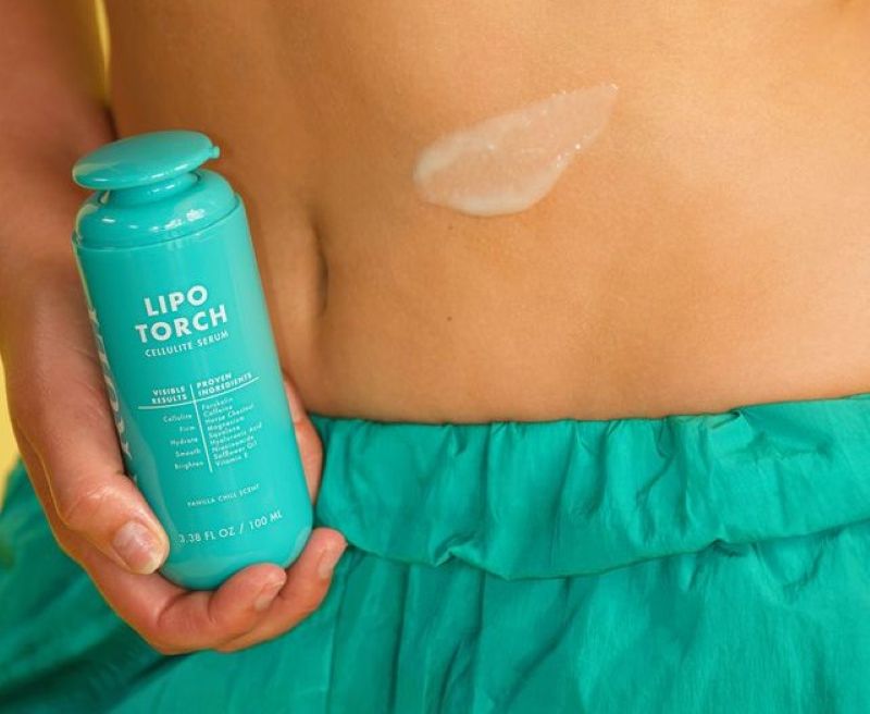 loose skin after pregnancy | A person holds a turquoise bottle of Truly Lipo Torch cellulite serum next to their stomach, where a dollop of the product is swiped onto the skin.