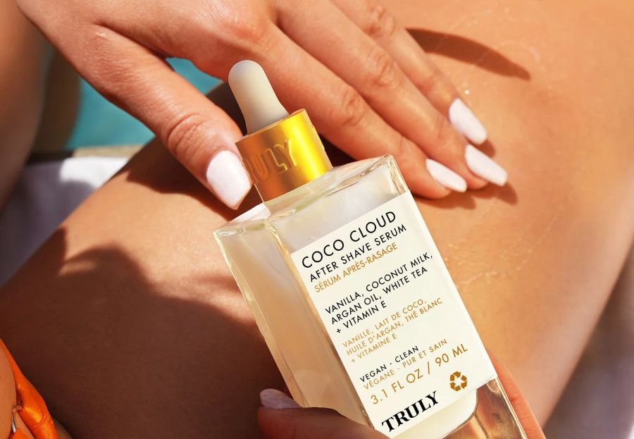 milky skin product | A person holds an opaque serum bottle - Truly coco cloud serum - while applying it to leg