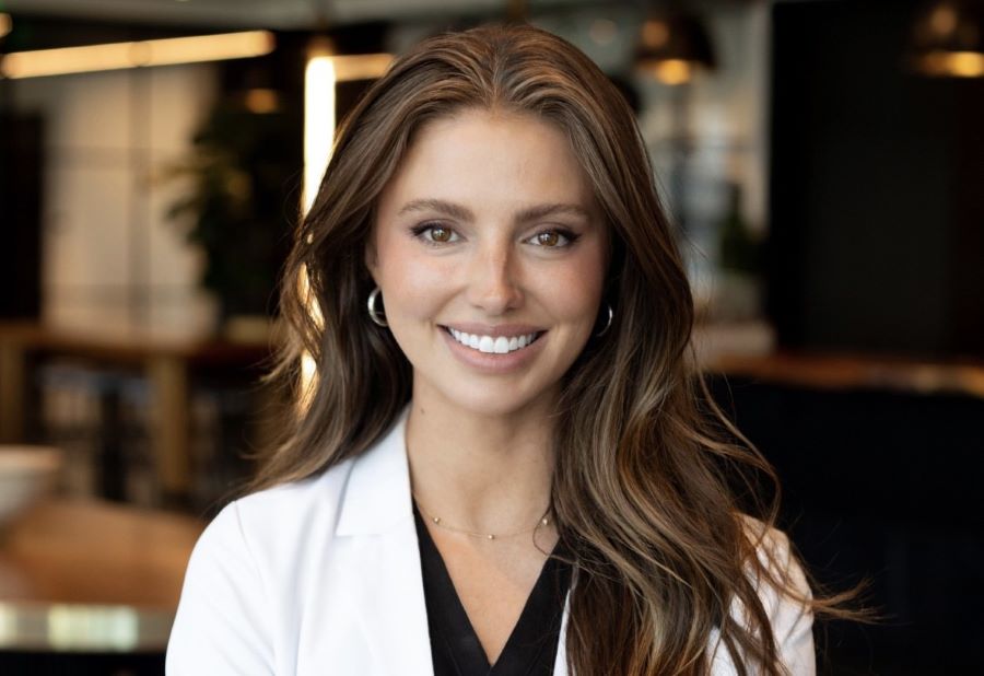 botox vs fillers | A young woman in white professional coat smiles as she looks directly at the camera