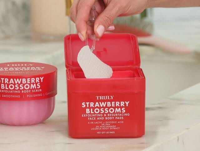 PHA pads | A person uses tweezers to lift a textured white exfoliation pad out of an open red container labeled 