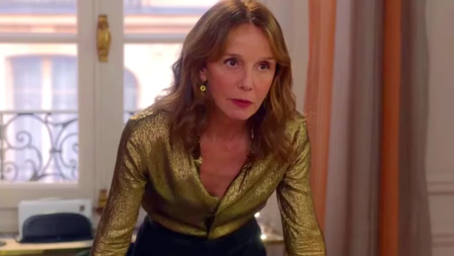 Philippine Leroy Beaulieu leaning on desk wearing gold sparkly shirt in emily in paris scene | Philippine Leroy-Beaulieu skincare routine