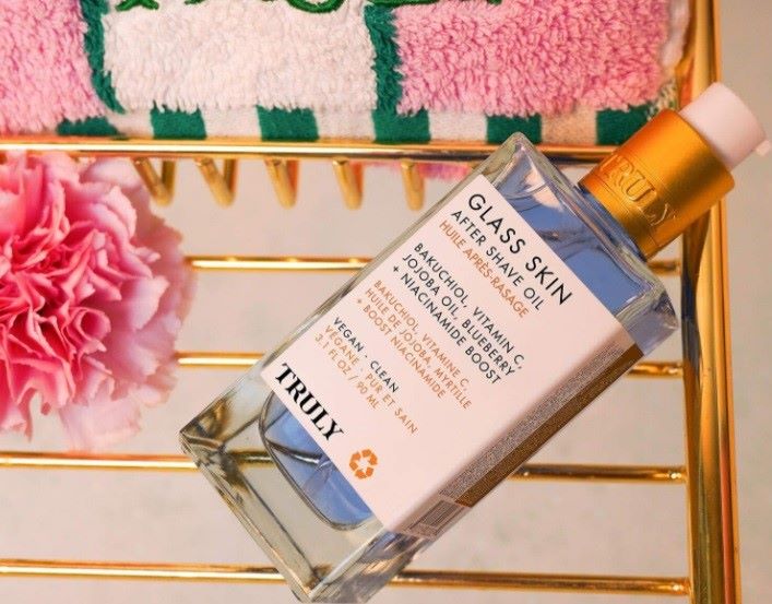 jojoba oil for skin | A bottle of truly's glass skin after shave oil lies on gold bath rack