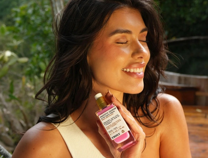 what are AHAs - Woman smiles with eyes closed, holding bottle of Truly's smooth legend serum