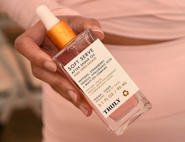 Closeup of woman's hand holding Truly's Soft Serve After shave oil with peptides, strawberry, vanilla and hyaluronic acid | what is hyaluronic acid 