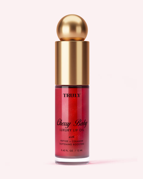 A clear tube of Truly Beauty Luxury Peptide Lip Oil with a gold cap and round top, featuring red lip oil inside and product details in black and gold text on the front.