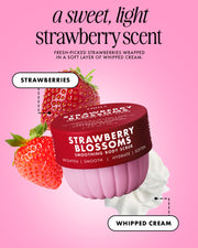 A pink promotional graphic for a strawberry-scented body scrub. A jar labeled 'Strawberry Blossoms' is shown with two strawberries and a swirl of whipped cream on a pink background.