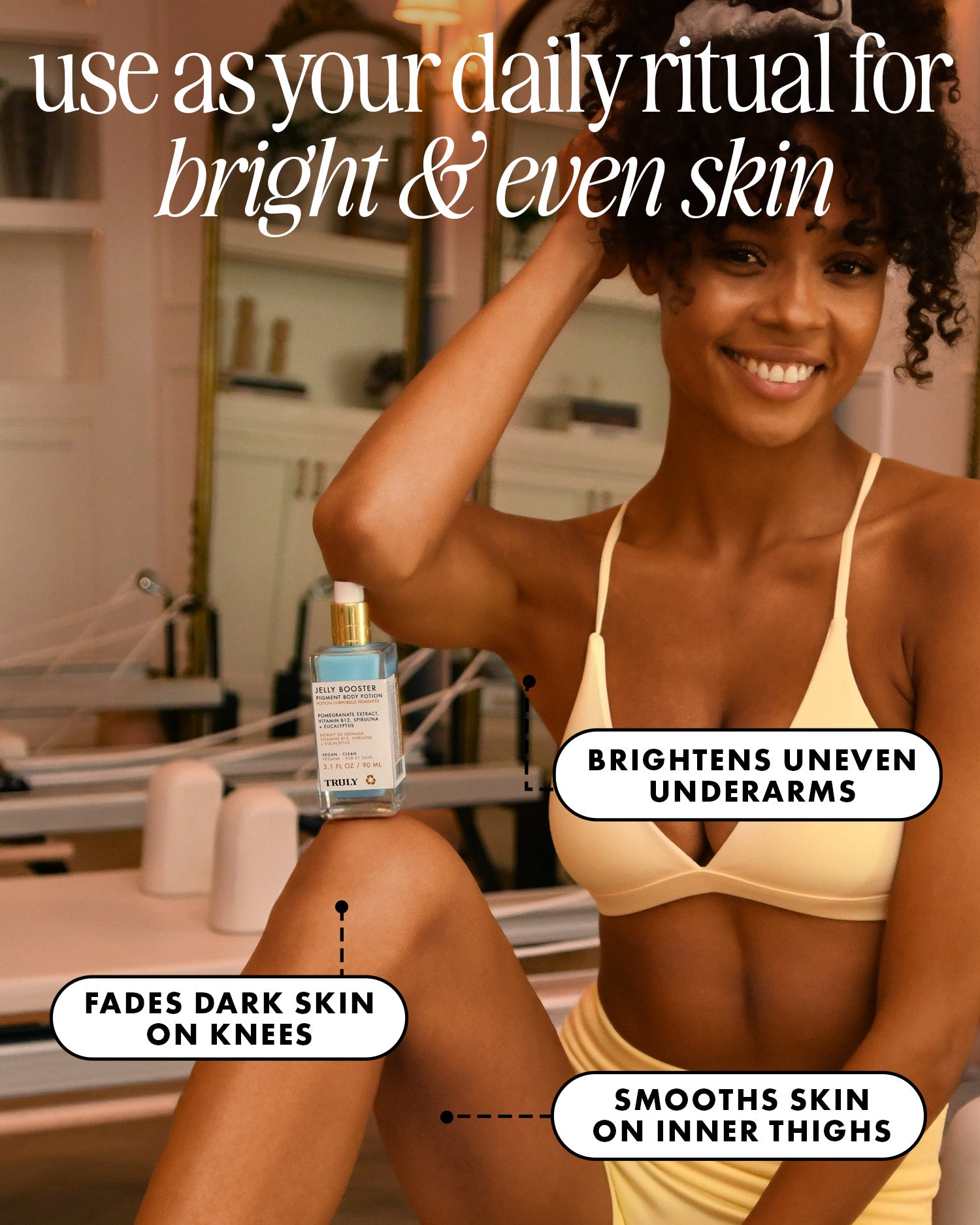 A smiling woman in a yellow bikini sits indoors, holding her leg. She displays Truly Beauty's Jelly Booster Pigment Body Potion, which helps brighten underarms, fade dark knees, lighten hyperpigmentation, and smooth inner thighs.