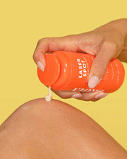 Person applying a product from an orange container labeled 'Laser Spot' on their leg against a yellow background