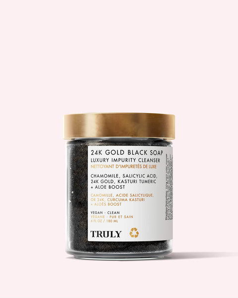 A glass jar of 24K Gold Black Soap Luxury Impurity Cleanser by Truly Beauty, with a gold lid and label noting anti-aging ingredients such as chamomile, salicylic acid, 24K gold, turmeric, and African black soap.