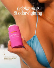 A woman in a blue top applies Truly Beauty’s Unicorn Fruit Skin Brightening and Smoothing Deodorant, featuring an aluminum-free, odor-fighting formula with papaya enzymes, mango butter, and SymWhite 377 to target underarm discoloration.