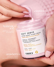 Una mano sostiene un frasco abierto de la Crema After Shave Plump de Truly Beauty, revelando su fórmula hidratante de color rosa. Contiene péptidos, ácido hialurónico y fresa para cuidar la piel y reducir las imperfecciones.