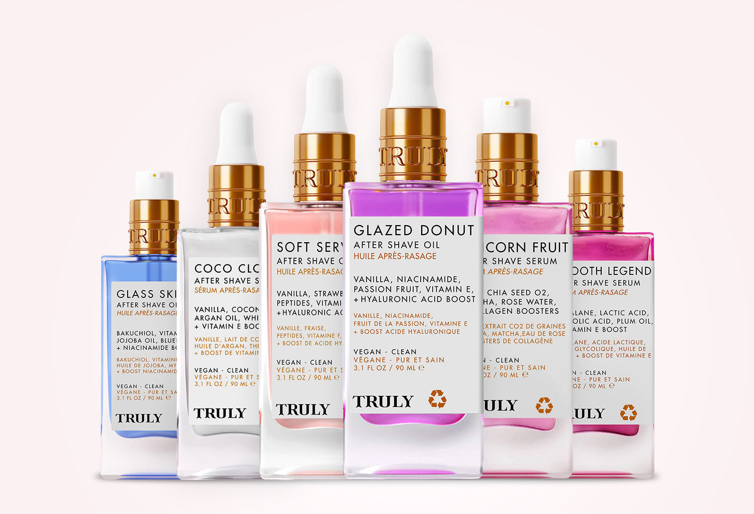 Six TRUELY brand shave and skincare bottles arranged in a row against a pale pink background. The bottles include Glass Ski, Coco Clo, Soft Series, Glazed Donut, Corn Ruth, and Tooth Legend, with white, blue, pink, and peach-colored bottles and gold caps.
