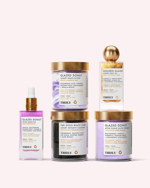 Annas Ultimate Routine by Truly Beauty is displayed against a light pink background. The collection, featuring creams, serum, and black cleanser in jars and a dropper bottle with white labels and gold accents, delivers radiant skin.