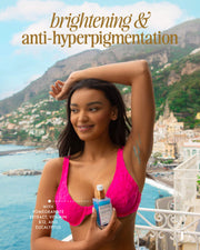 A woman in a bright pink bikini smiles and raises her arm, holding Truly Beauty's Jelly Booster Pigment Body Potion. Brightening & anti-hyperpigmentation text appears as a coastal town and mountains fill the background.