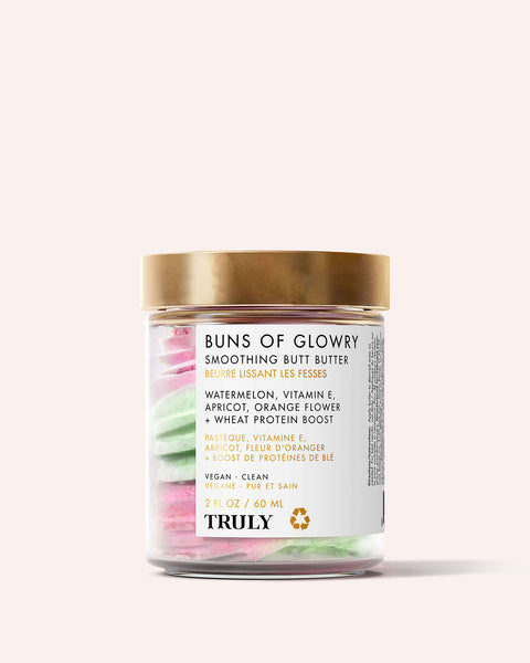 A clear jar with a gold lid labeled Buns of Glowry Smoothing Butt Butter by Truly Beauty features watermelon extract, vitamin E, apricot, orange flower, and wheat protein. Inside is pink and green smoothing cream.