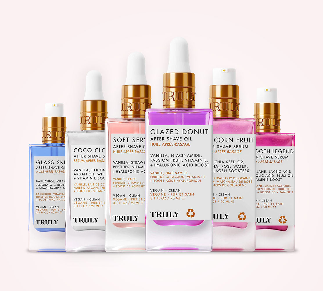 Six TRUELY brand skincare bottles arranged in a row against a light pink background. The bottles contain liquids in shades of blue, beige, peach, white, and pink, and are topped with gold caps.