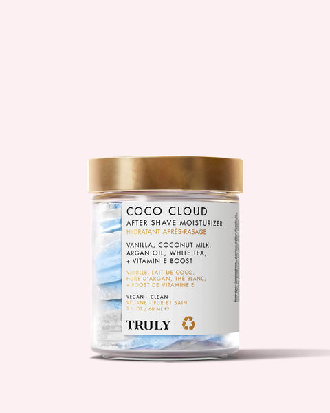 A clear jar with a gold lid labeled Truly Beauty Coco Cloud After Shave Moisturizer holds blue and white swirl cream cubes. The label highlights nourishing shea butter, coconut milk, and argan oil.