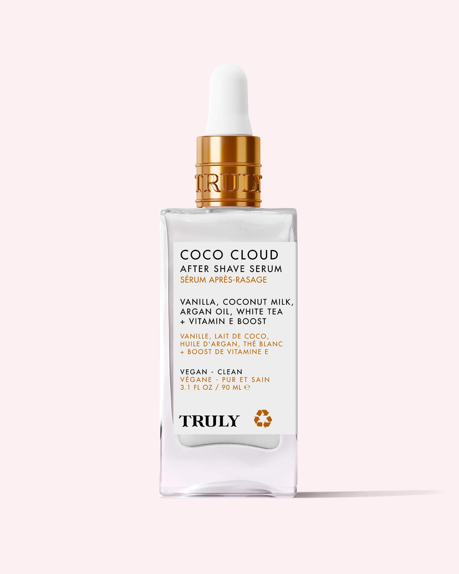A clear glass dropper bottle labeled Coco Cloud After Shave Serum by Truly Beauty, featuring hydrating argan oil, coconut milk, vanilla, white tea, and vitamin E. The bottle sits on a light pink background.
