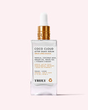 A clear glass dropper bottle labeled Coco Cloud After Shave Serum by Truly Beauty, featuring hydrating argan oil, coconut milk, vanilla, white tea, and vitamin E. The bottle sits on a light pink background.