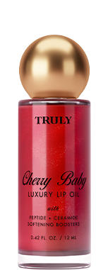 A bottle of Truly Lip Oil Cherry Baby with a gold cap and pink shimmery liquid, two cherries in front. Pink lip oil is swatched in the background.