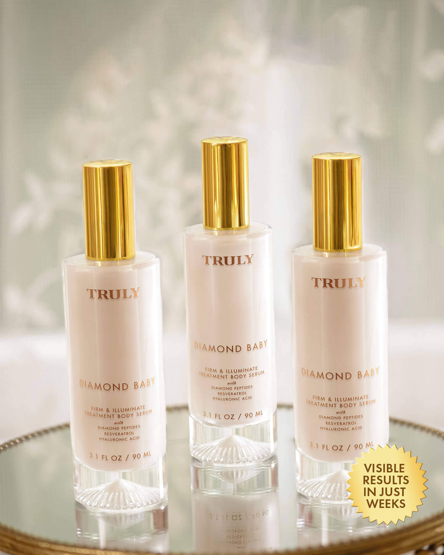 Three bottles of Truly Diamond Baby skincare product on a reflective surface with a soft light background.