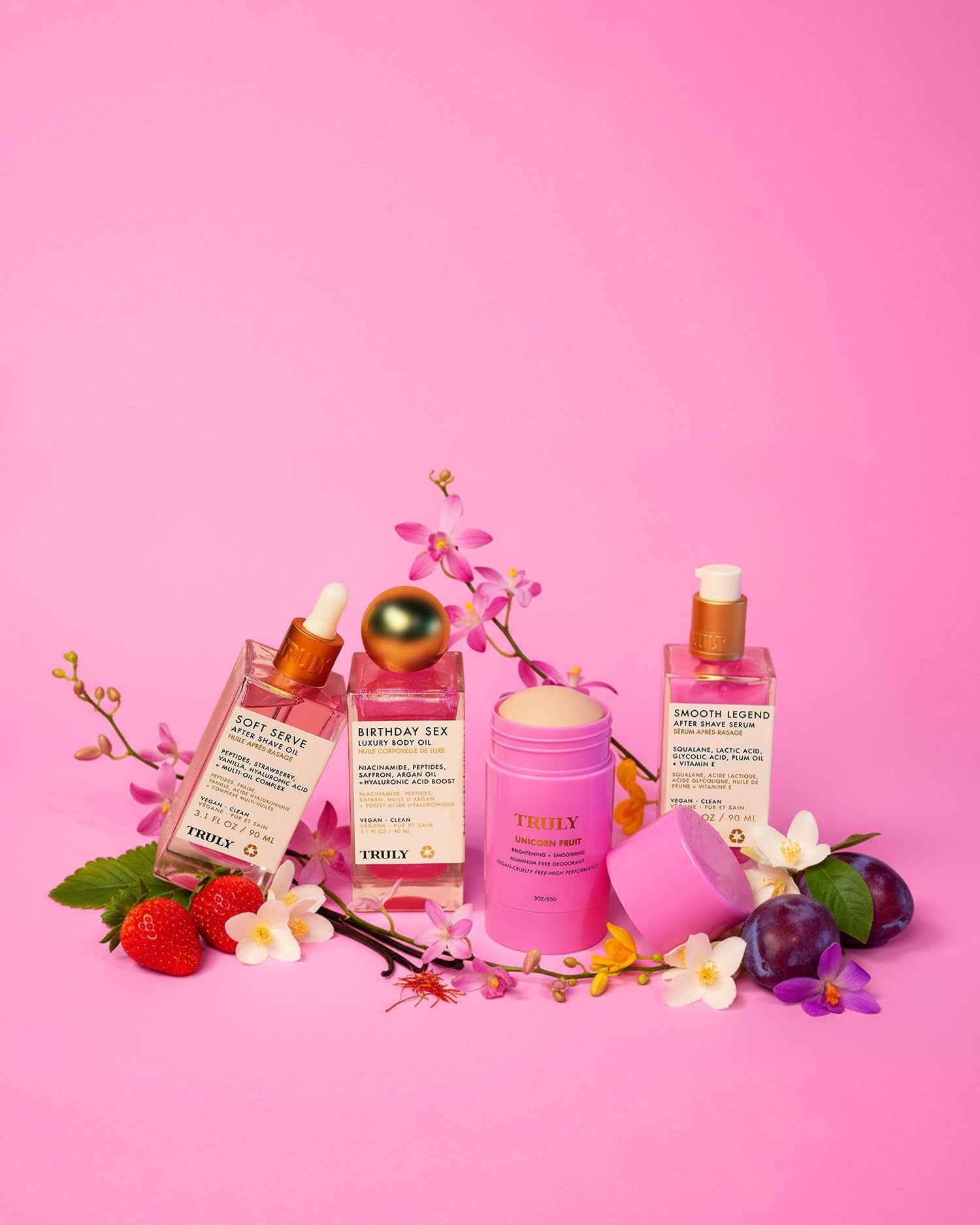 Tiktok Pink Routine by Truly Beauty—three pink bottles and a stick container—are artfully arranged with strawberries, plums, and orchids on a pink background, creating a vibrant skincare scene.