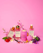 Tiktok Pink Routine by Truly Beauty—three pink bottles and a stick container—are artfully arranged with strawberries, plums, and orchids on a pink background, creating a vibrant skincare scene.