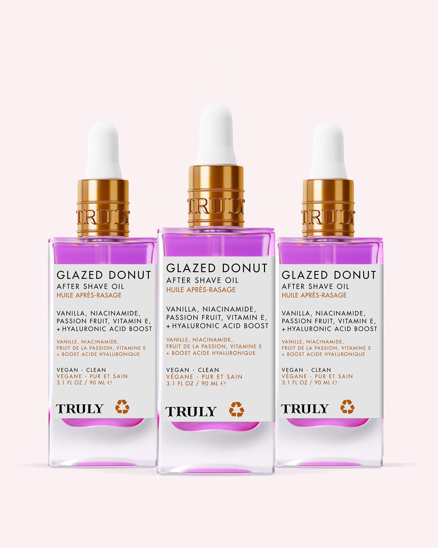Three bottles of Truly Beauty’s Glazed Donut After Shave Oil (Copy), each with a gold dropper cap and clear label, are set against a light pink background—ideal for post-shave hydration and preventing ingrown hairs.