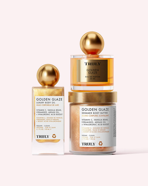The Golden Glaze Luxury Trio from Truly Beauty features hydrating essentials—a body oil, shimmer body butter, and eau de parfum—in gold-accented jars and bottles with round gold caps, displayed on a light background.